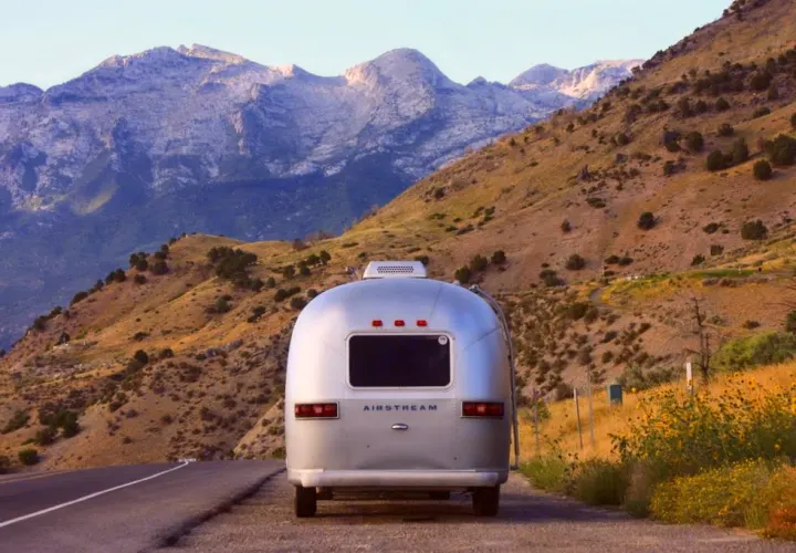An Airstream RV rental: Silver trailer parked roadside, with majestic mountains and hilly terrain in the background.. Airstream Trade Wind 1976