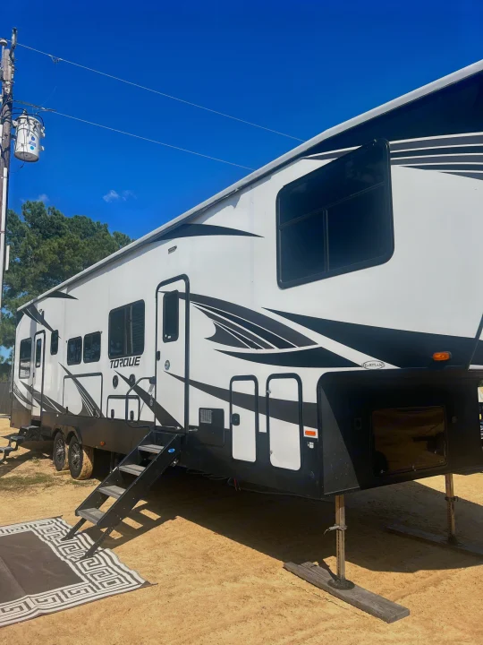 White and black Heartland Torque fifth-wheel toy hauler rv rental on sand, ready for camping fun under blue sky.. Heartland Torque 2020