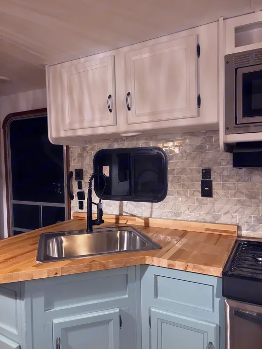 Modern RV rental kitchen with butcher block countertops, light blue cabinets, and subway tile backsplash.. Gulf Stream Conquest 2016