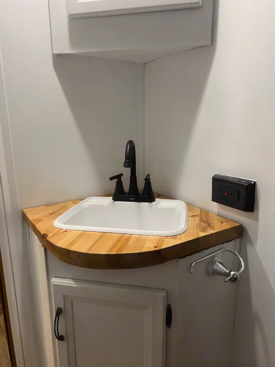 A compact RV rental bathroom with a corner sink, wooden countertop, black faucet, and wall outlet.. Gulf Stream Conquest 2016