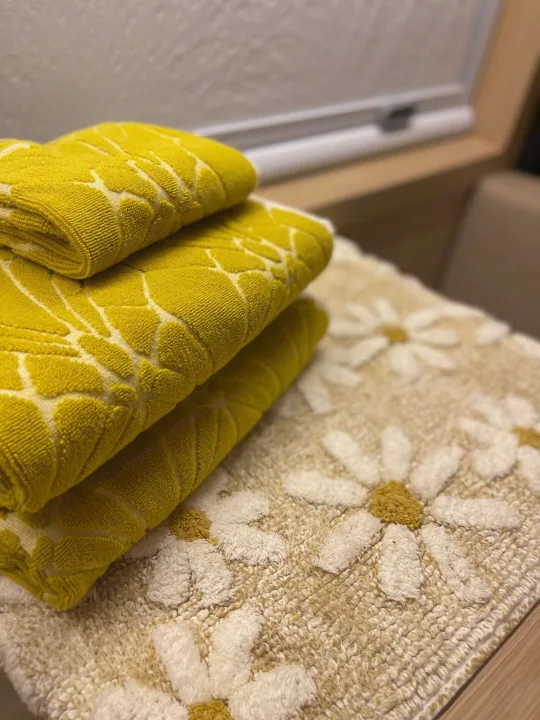 Close-up of bright yellow towels with a leaf pattern, stacked on a beige daisy bath mat, in a cozy rv rental.. Dodge Ram Promaster 3500 C/V HR 159 EXT 2023