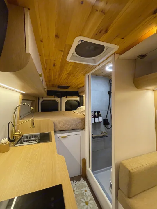 Inside a modern camper van (RV rental) featuring a compact kitchen with a gold faucet, a cozy bed, and a sleek shower.. Dodge Ram Promaster 3500 C/V HR 159 EXT 2023