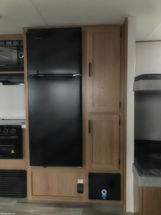 This RV rental shows a compact kitchen with a black refrigerator, microwave, oven, wood cabinets, and built-in bunk beds.. Forest River Avenger LE 2022