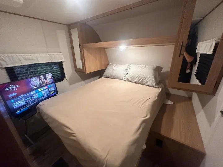 Relax in this RV rental bedroom featuring a comfy bed, overhead storage, a window, and a TV with streaming services.. Forest River Avenger LE 2022