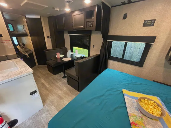 Inside a comfortable rv rental: bed with popcorn, dining booth, kitchen counter, and bunk beds with a sweet dog.. Jayco Jay Flight 2023