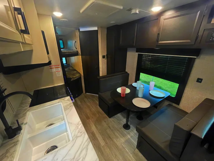 RV rental interior featuring a modern kitchen with sink, cozy dinette, and bunk beds, offering a spacious layout.. Jayco Jay Flight 2023