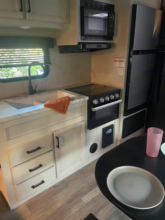 Modern RV rental kitchen with sink, stove, microwave, refrigerator, and light wood cabinets, ready for your trip.. Jayco Jay Flight 2023