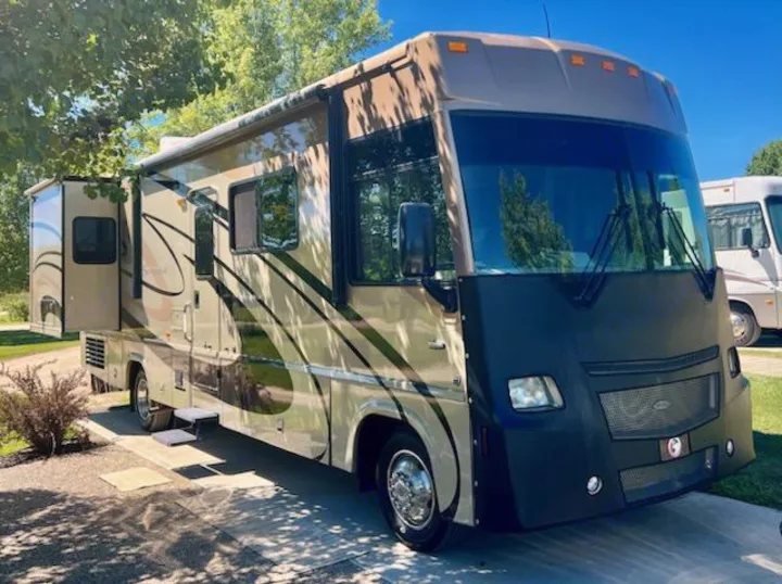 Large tan RV rental with extended slide-out, parked outdoors, ready for your next travel adventure.. Itasca Sunrise 2008