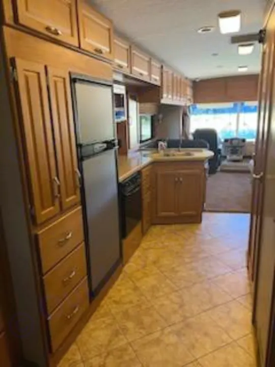 This spacious RV rental interior features a kitchen with wood cabinets, refrigerator, and tiled floor, leading to the living area.. Itasca Sunrise 2008