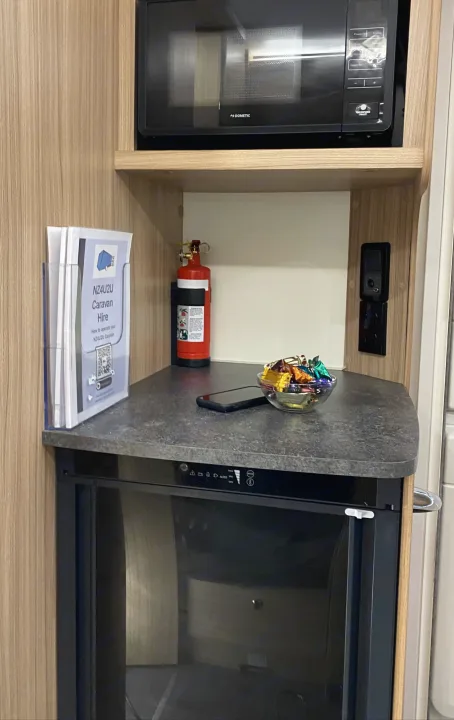 Inside an RV rental: Dometic microwave, compact fridge, fire extinguisher, and a candy bowl on the counter, with rental info.. Bailey x 2022