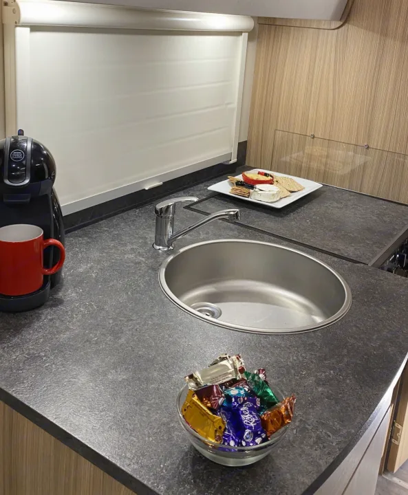 Bright RV rental kitchen with Nescafé Dolce Gusto machine, sink, cheese board, & bowl of chocolates on speckled counter.. Bailey x 2022