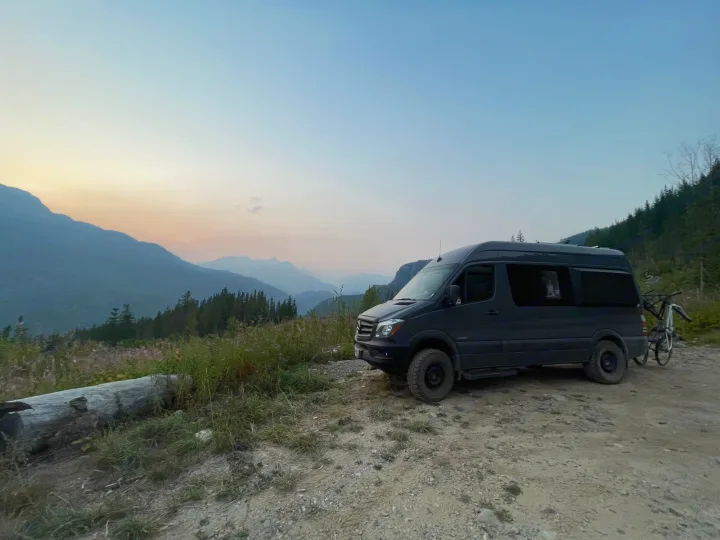 Adventure awaits with this dark gray Sprinter camper van parked on a mountain dirt road at dusk, perfect for an RV rental.. Mercedes Sprinter 2016
