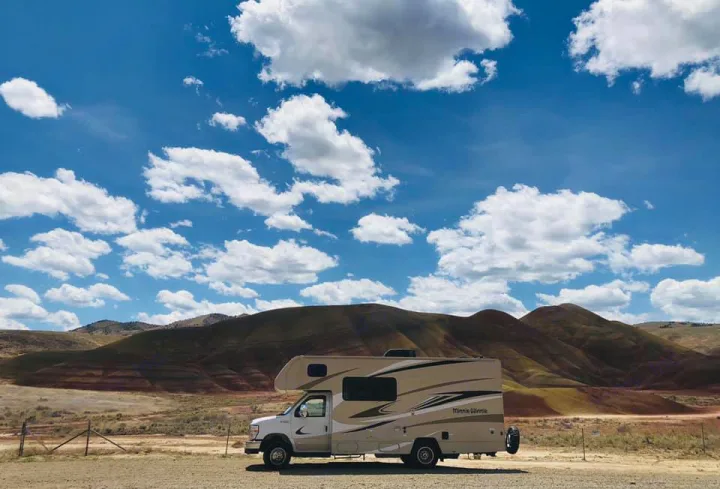 An RV rental (Minnie Winnie) parked at a scenic overlook with colorful striped hills and a blue, cloudy sky.. Winnebago Minnie Winnie 2020