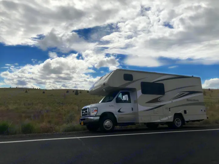 Minnie Winnie RV rental on a scenic road trip. Beige motorhome parked roadside under a big, cloudy sky.. Winnebago Minnie Winnie 2020