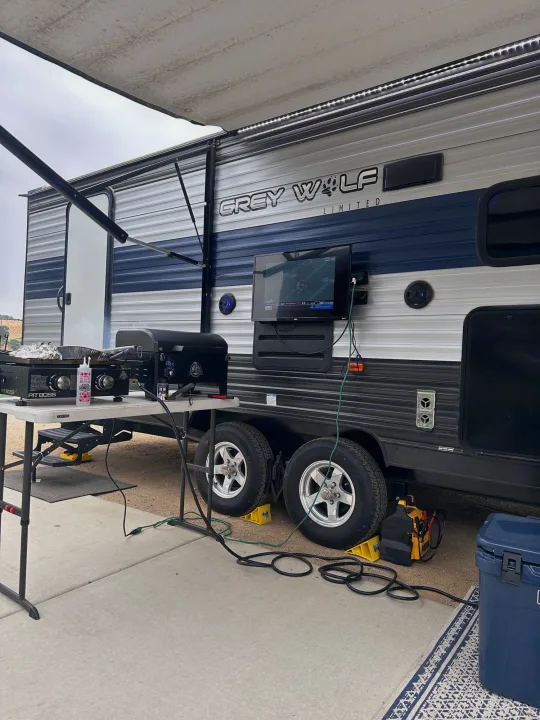An RV rental campsite showcasing an outdoor kitchen with a grill, a TV mounted on the side, and a large awning.. Forest River Cherokee Grey Wolf 2021