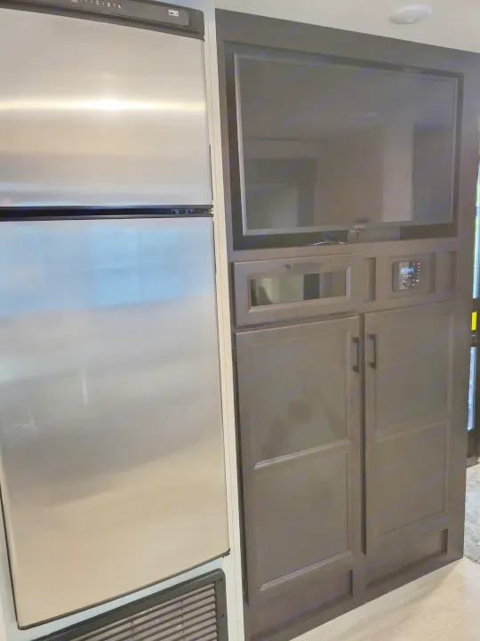 RV rental interior: Stainless steel fridge flanks dark entertainment center with TV, stereo, and storage. Modern, compact living area.. Jayco Jay Flight Baja Edition 2023