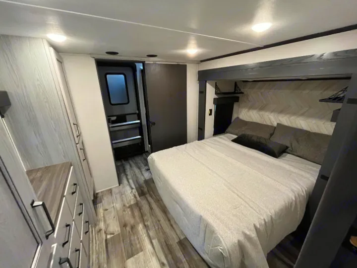 Modern RV rental bedroom featuring a comfortable bed, stylish herringbone headboard, and ample storage.. Keystone RV Montana High Country 2023