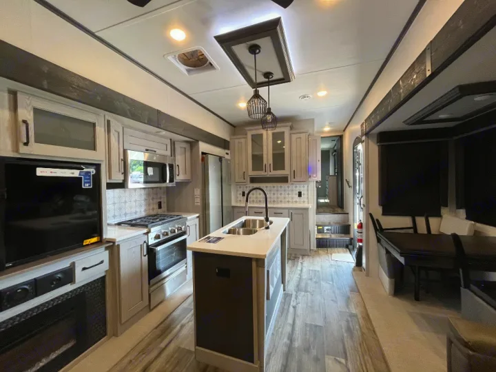 Spacious, modern RV rental interior featuring a full kitchen, island, living area, and dining booth. Ideal for travel.. Keystone RV Montana High Country 2023