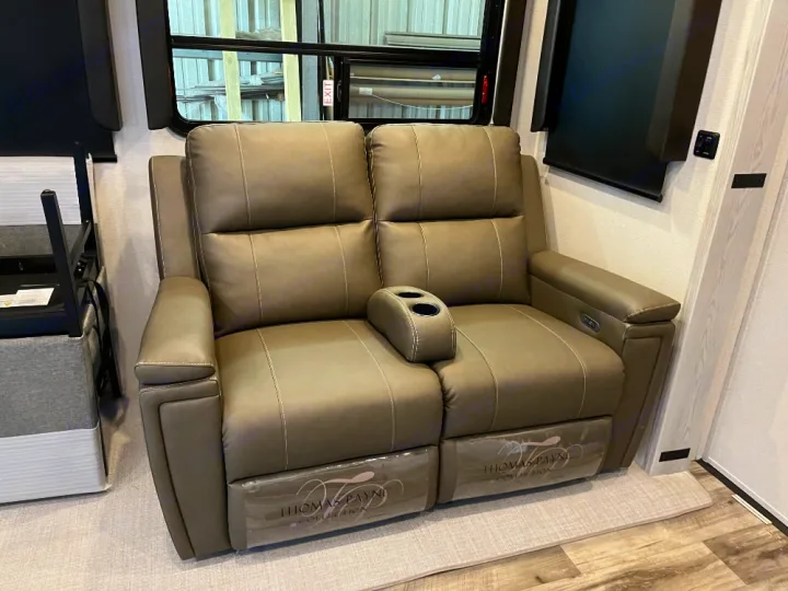 Taupe two-person recliner sofa with cupholders inside an RV, providing comfort for your rv rental trips.. Keystone RV Montana High Country 2023
