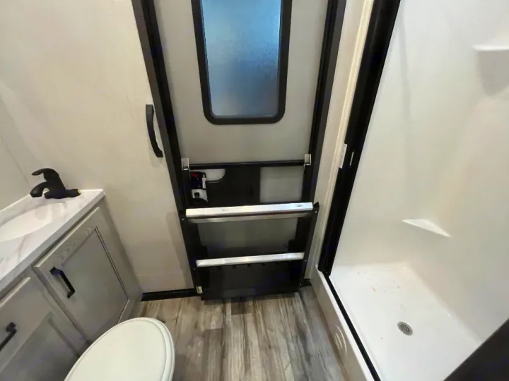 This RV rental bathroom showcases a compact design with a sink, toilet, and shower stall, plus a convenient entry door with steps.. Keystone RV Montana High Country 2023