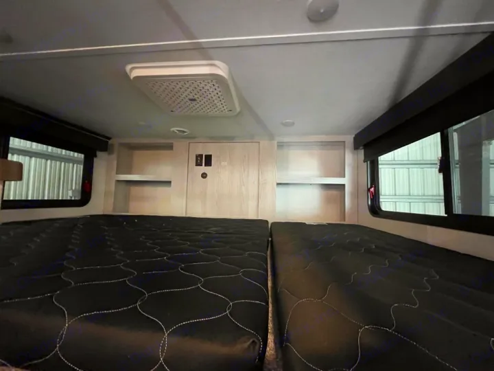 Cozy RV rental sleeping area with two black quilted beds, side windows, overhead AC, and built-in storage.. Keystone RV Montana High Country 2023