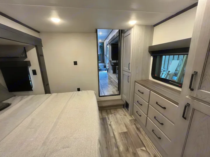 Step inside this modern RV rental! A comfortable bedroom with a large bed, dresser, storage, and a bright, inviting interior.. Keystone RV Montana High Country 2023