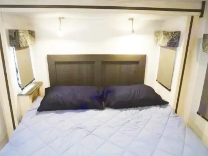 Cozy RV rental bedroom featuring a dark headboard, light blue bedding, and two dark pillows. Ideal for your next road trip.. Forest River Sunseeker Classic 2023