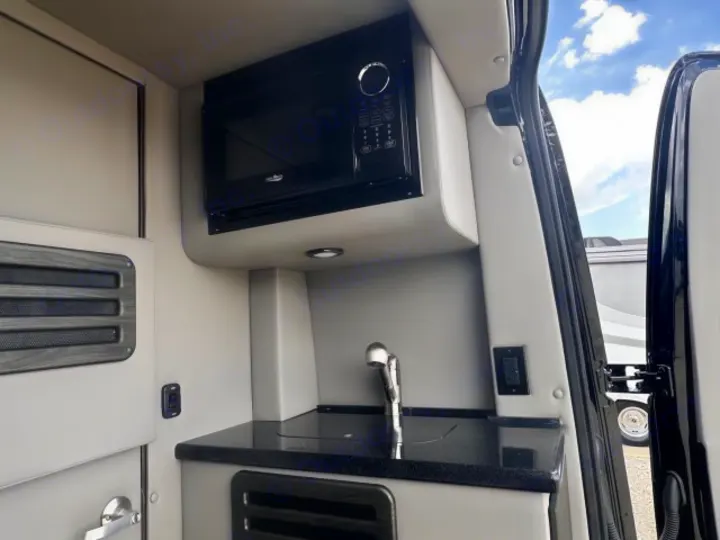 Explore RV rental amenities: a compact kitchen with a built-in microwave, sink, and dark counter.. Midwest Automotive Designs Midwest Automotive Designs Class B 2024