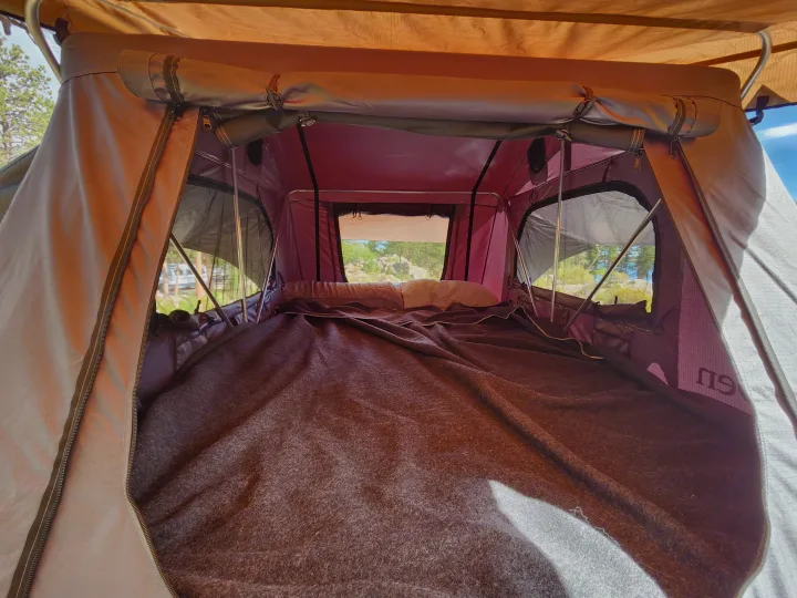 Inside a spacious RV rental rooftop tent: a comfortable bed and open windows with nature views.. Modern Buggy Little Buggy 10LR 2024