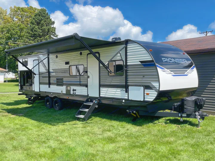 New Pioneer travel trailer RV rental, parked on green grass with its awning extended under a clear sky.. Heartland RVs Pioneer 2022