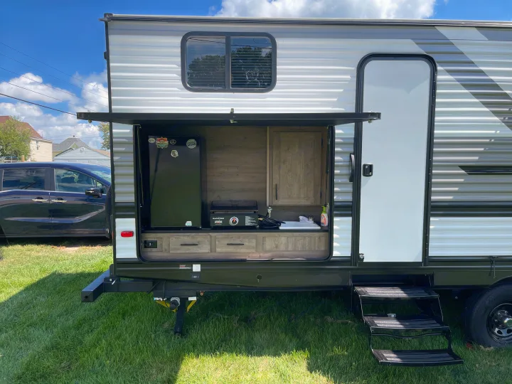 Outdoor kitchen of an rv rental revealed on a sunny day, complete with fridge, griddle, and sink for convenient outdoor cooking.. Heartland RVs Pioneer 2022