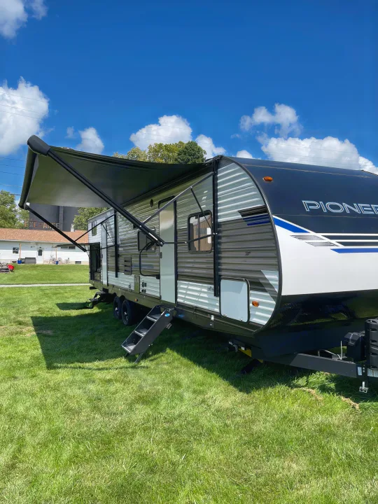 Spacious Pioneer travel trailer RV rental parked on sunny grass. Awning extended, ready for outdoor adventure.. Heartland RVs Pioneer 2022