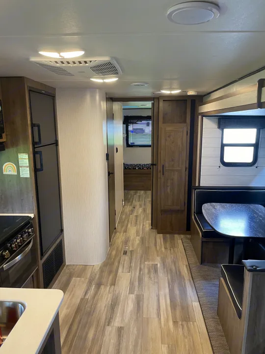 Bright rv rental interior: kitchen with stove/fridge, dining booth, and rear bedroom. Functional and cozy.. Heartland RVs Pioneer 2022