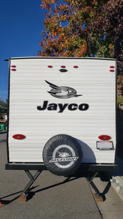 White Jayco travel trailer, with its spare tire and stabilizing jacks. A great option for your next RV rental adventure.. Jayco Jay Flight SLX Baja Edition 2022