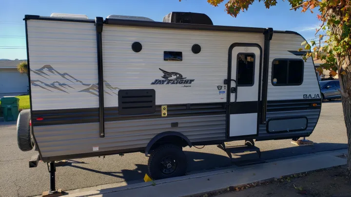 A white and gray Jay Flight Baja travel trailer, an excellent RV rental option, is parked on a sunny street.. Jayco Jay Flight SLX Baja Edition 2022