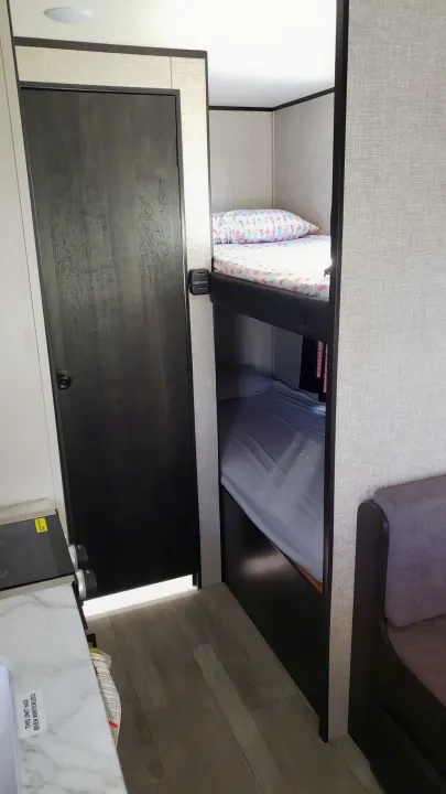 RV rental interior showing cozy bunk beds, a dark wood door, and a hint of the kitchen area.. Jayco Jay Flight SLX Baja Edition 2022