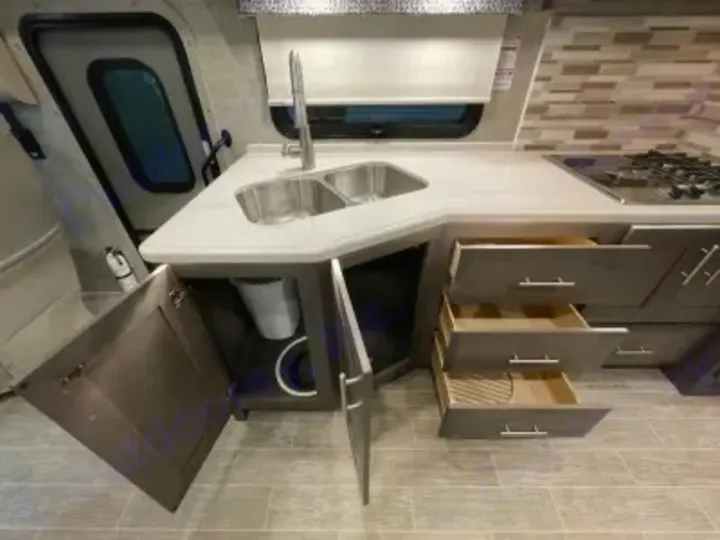 Modern RV rental kitchen featuring a double sink, gas stovetop, pull-out drawers, and under-sink storage.. Thor Miramar 2022