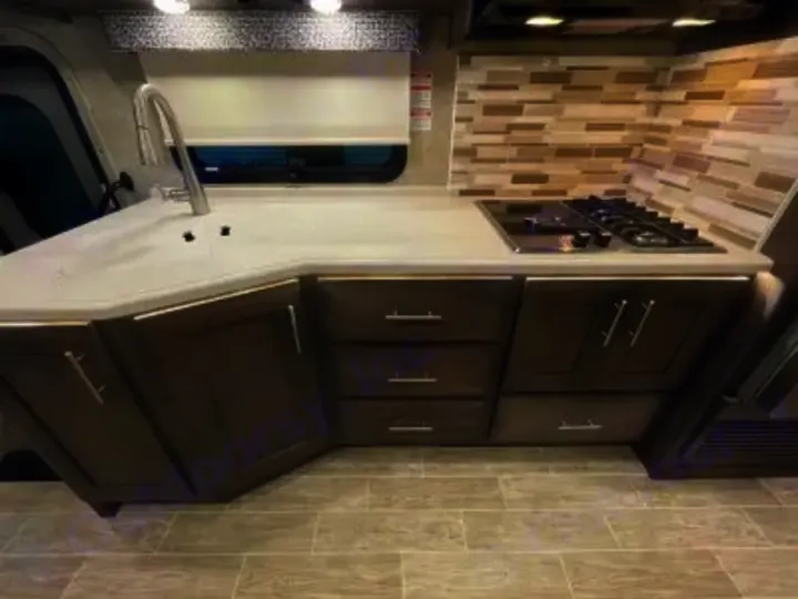 Compact RV rental kitchen features a light counter, sink, stovetop, and dark cabinetry with under-cabinet lighting.. Thor Miramar 2022