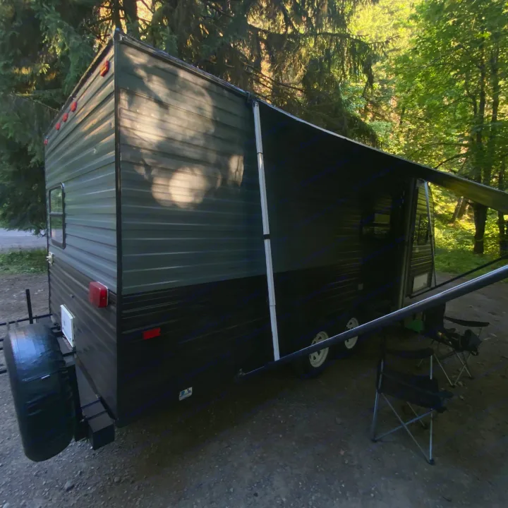Perfect RV rental getaway! Dark travel trailer with extended awning and camping chairs under lush forest trees.. Fleetwood Prowler 1996