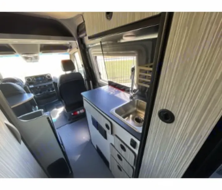 RV rental: Bright, modern camper van interior, showcasing a compact kitchen with sink and organized cabinetry, plus the driver's cab.. Winnebago Revel 2023