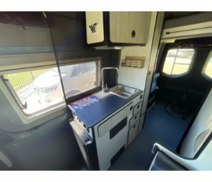 Explore this RV rental's camper van interior: a compact kitchen with sink, counter, & cabinets, plus windows for scenic views.. Winnebago Revel 2023