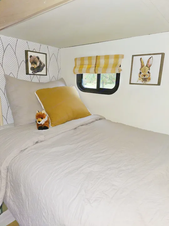 Relaxing RV rental bedroom featuring soft grey bedding, cute animal art, and a charming yellow plaid blind.. Forest River Coachmen Freelander 2014