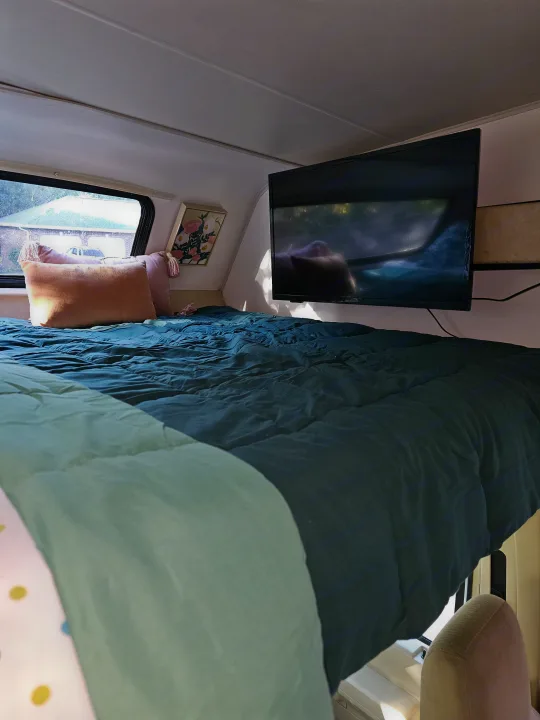 Cozy RV rental sleeping space featuring a bed with teal bedding, peach pillows, and a mounted TV, ready for travel.. Forest River Coachmen Freelander 2014
