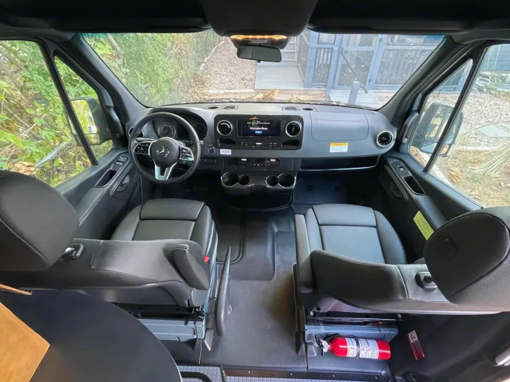 Experience a clean Mercedes-Benz Sprinter rv rental. Wide-angle view of the modern cockpit, dashboard, and front seats.. Winnebago Revel 2023