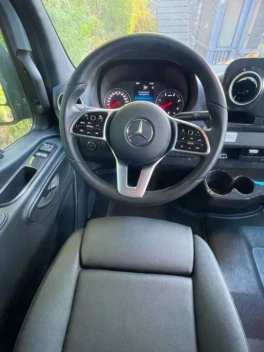 Inside a clean rv rental: Mercedes-Benz steering wheel, dashboard with 102°F, and comfortable driver's seat.. Winnebago Revel 2023