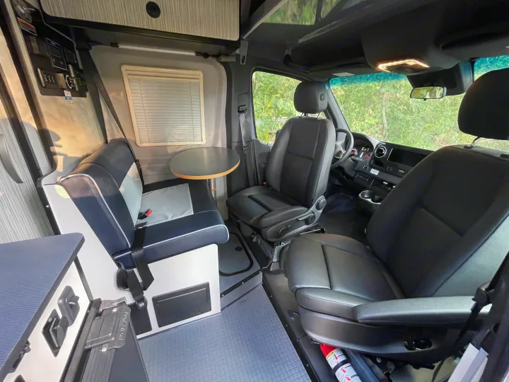 Explore this versatile rv rental interior: dining area with bench, swiveling front seats, overhead storage, and controls.. Winnebago Revel 2023