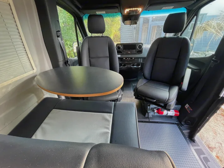 Interior of an RV rental featuring swivel seats, a dinette table, and safety equipment like a fire extinguisher.. Winnebago Revel 2023