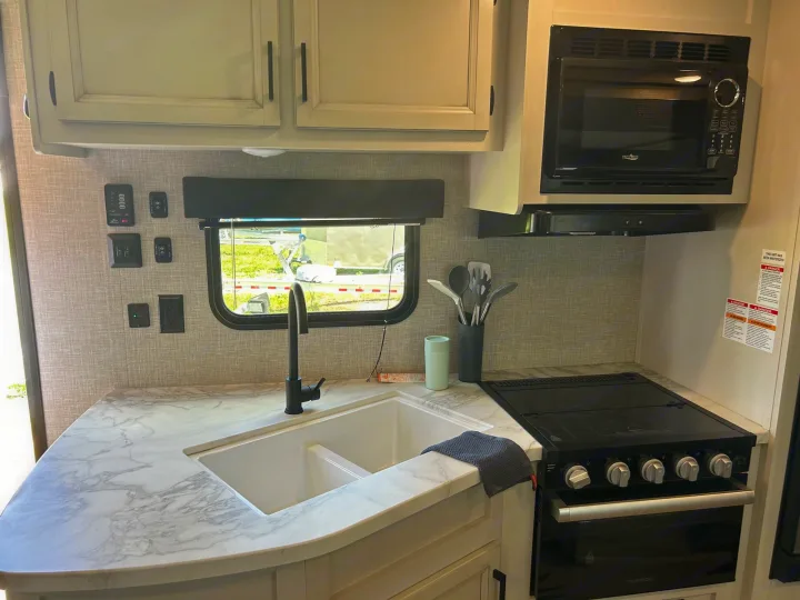 Inside an rv rental: Well-equipped kitchen with marble-look counter, double sink, black stove, microwave, and overhead cabinets.. Jayco Jay Flight 2023