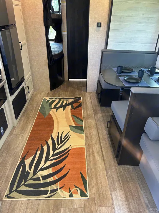 Clean RV rental interior showing a dinette, kitchen area, and bunk beds, with a patterned rug.. Jayco Jay Flight 2023