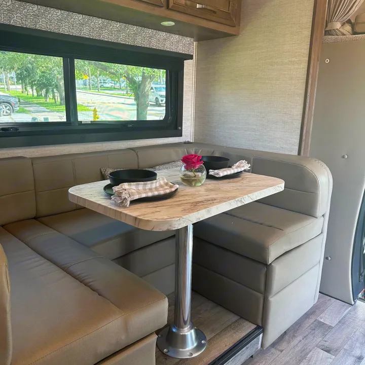 RV rental dinette: comfortable booth seating, a marble-look table set with bowls and a rose, offering outdoor views.. Jayco Melbourne 2022